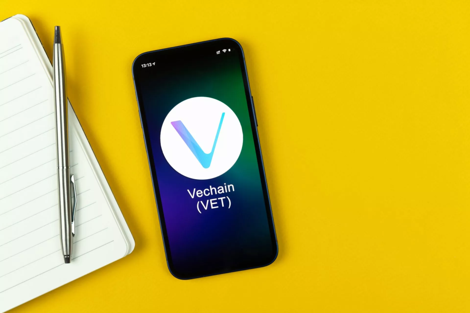 VeChain (VET) logo op smartphone naast notitieboek op gele achtergrond