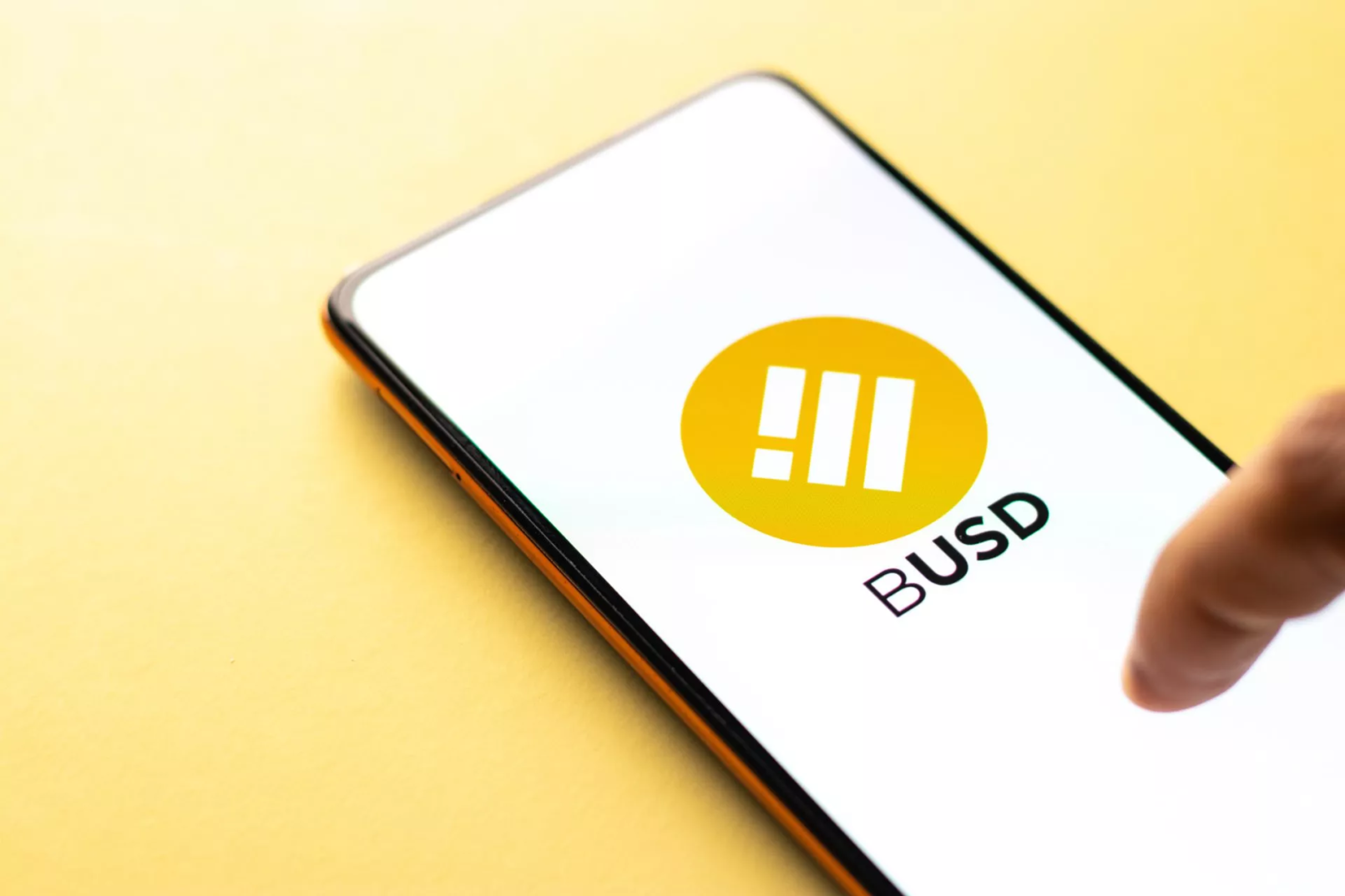 BUSD-logo op smartphone met vingeraanwijzing op gele achtergrond, symbool voor Binance stablecoin