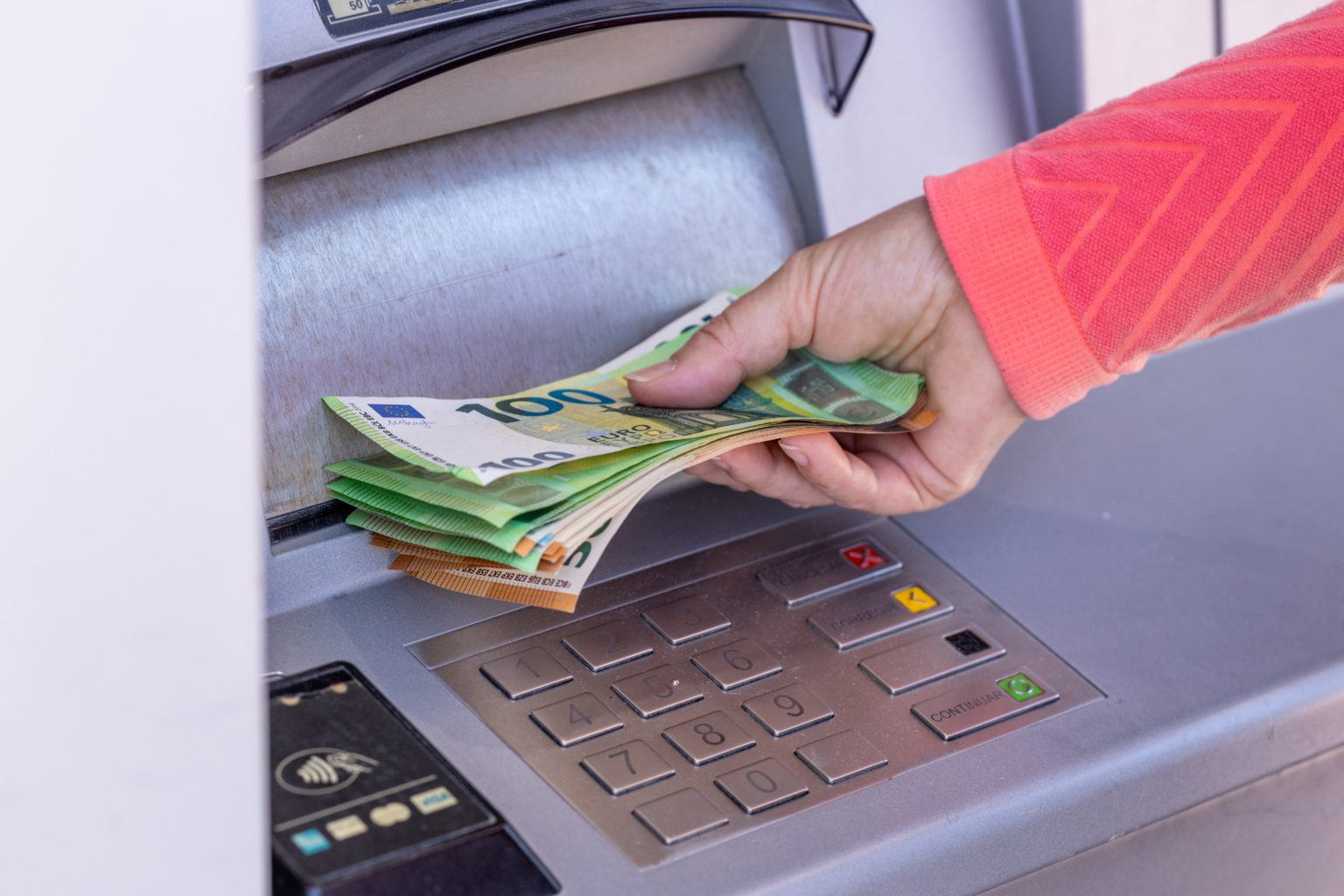 Hand pakt stapel eurobankbiljetten uit pinautomaat