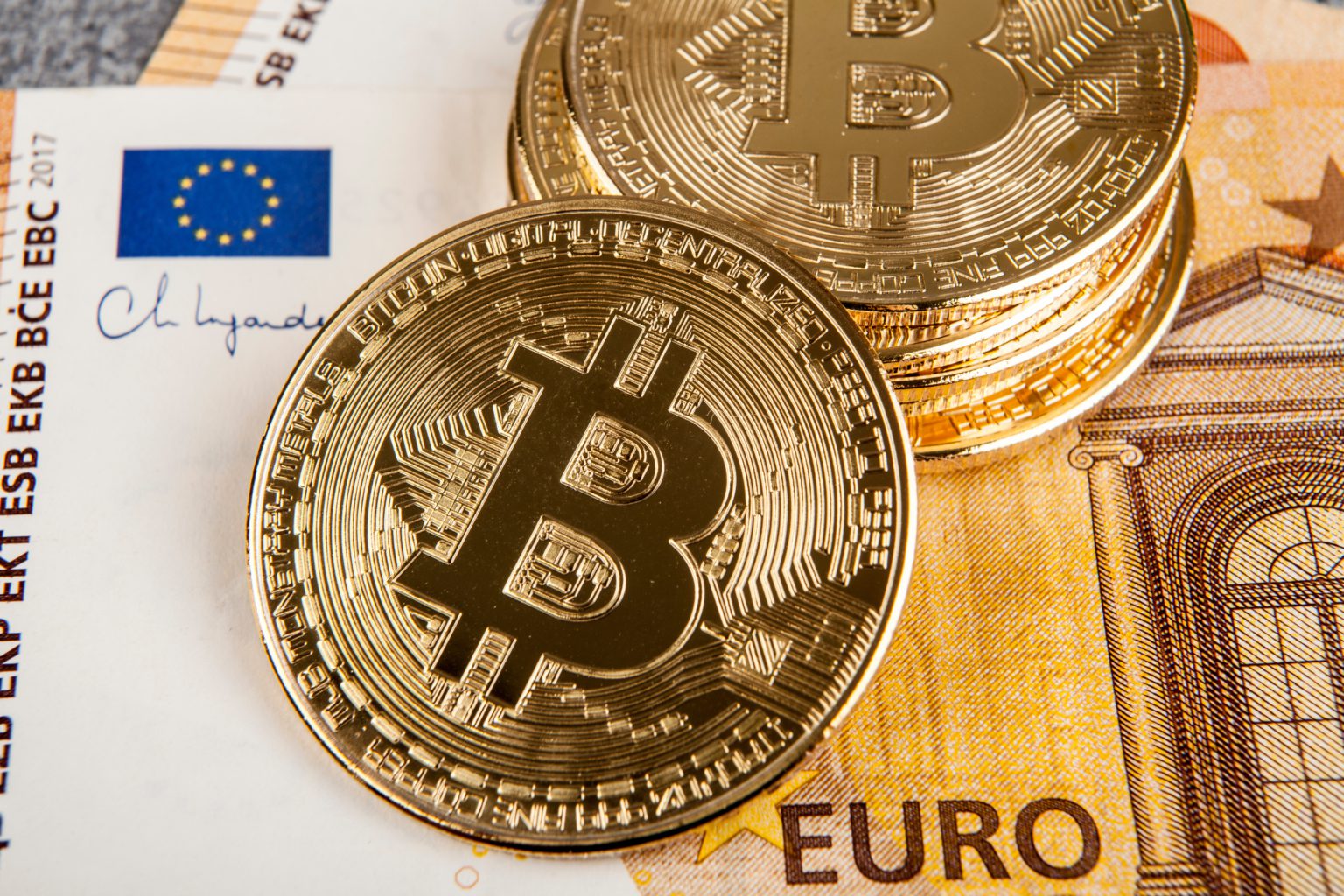 Stapel gouden Bitcoin munten op eurobiljet met EU-vlag zichtbaar