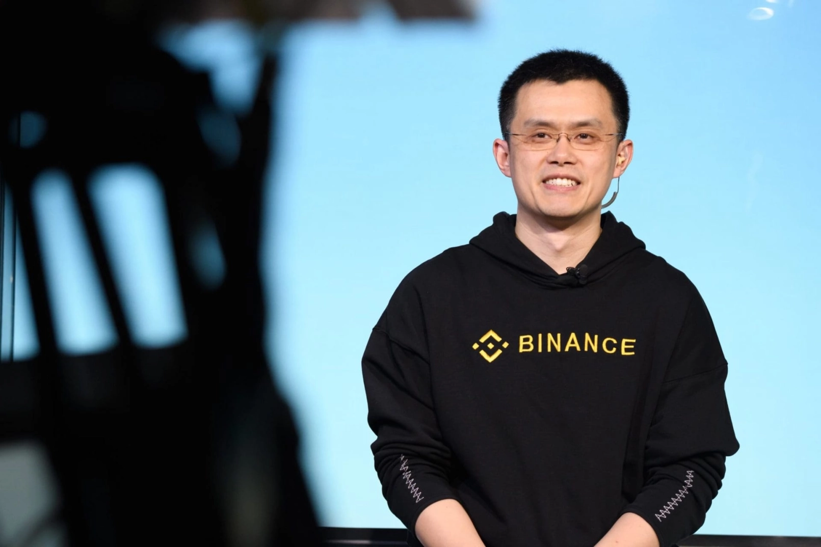 Changpeng Zhao im Binance-Pullover mit Mikrofon auf der Bühne bei einem Krypto-Event