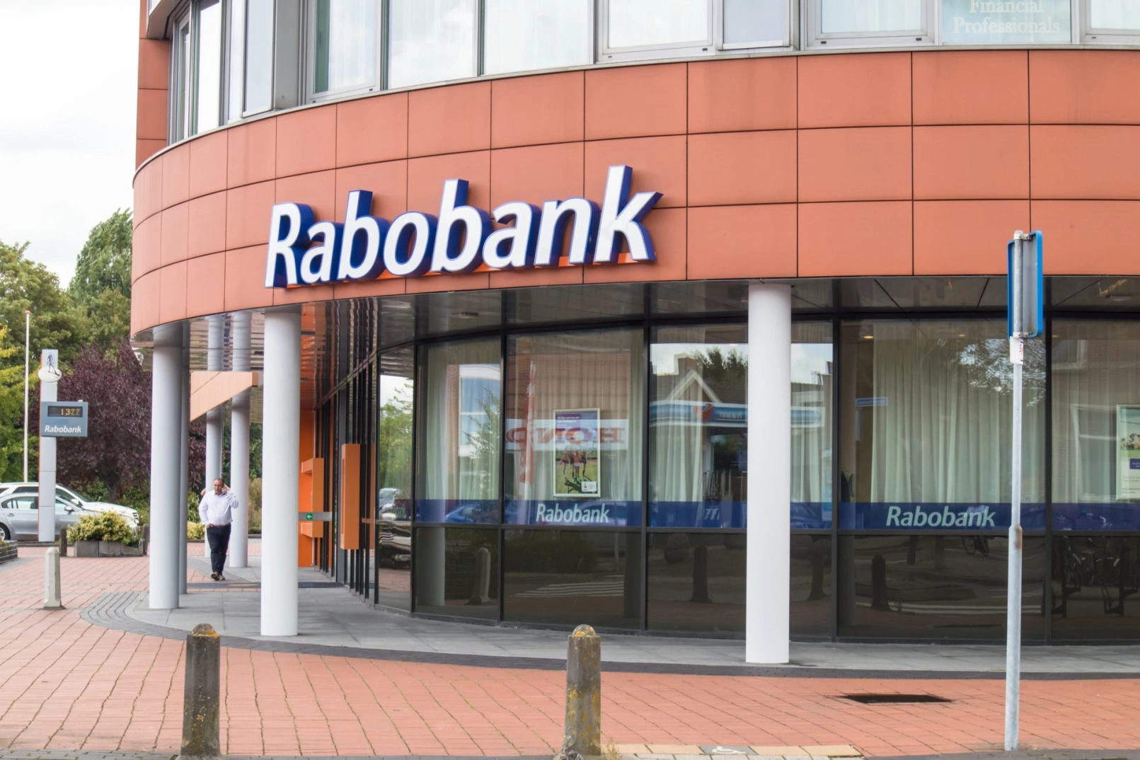 Fassade einer Rabobank-Filiale mit Logo und einem vorbeigehenden Mann auf dem Bürgersteig