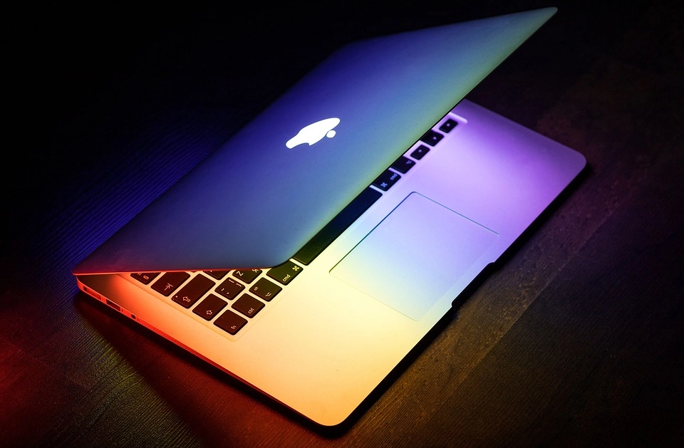 Halb geöffnetes MacBook mit regenbogenfarbener Tastaturbeleuchtung als Symbol für Technologie und Krypto