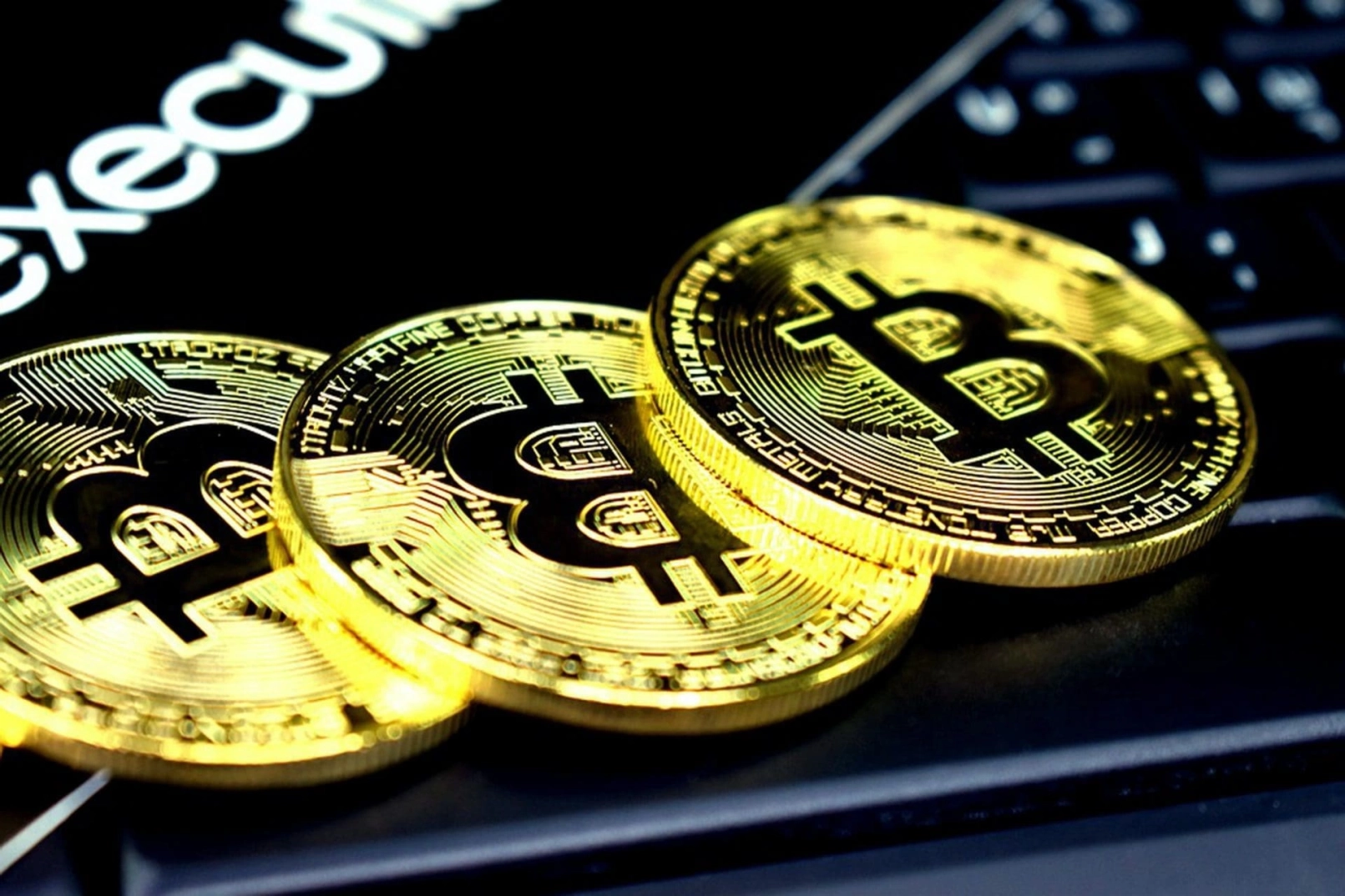 Tres monedas doradas de Bitcoin sobre un teclado con la palabra «executive» al fondo